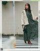 A woman in a green dress and a white coat is walking down the street.