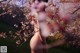 A naked woman standing in front of a flowering tree.