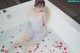 A woman sitting in a bathtub with rose petals on the floor.