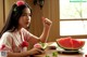 A woman sitting at a table eating a slice of watermelon.