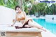 A woman in a bikini sitting on a lounge chair by a pool.